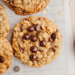 A close up of an oatmeal chocolate chip cookie on parchment paper.