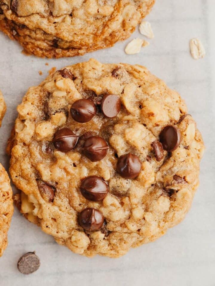 A close up of an oatmeal chocolate chip cookie on parchment paper.