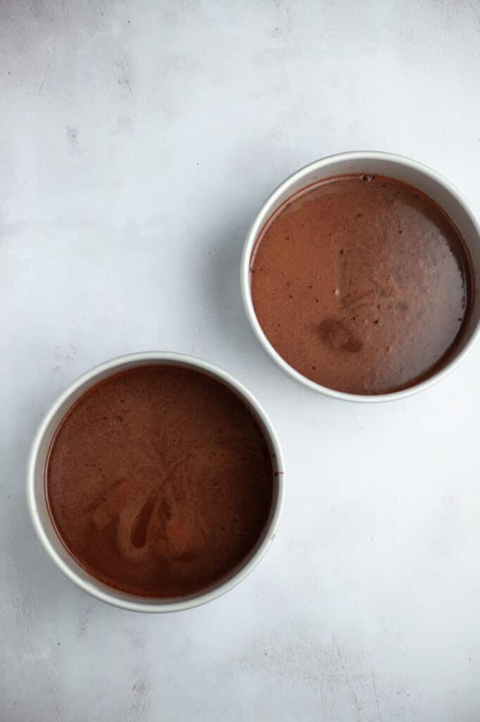 Two silver cake pans filled with dark brown cake batter