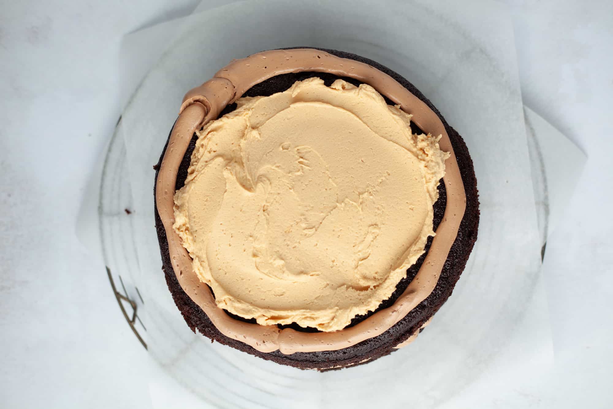 An overhead shot of a chocolate cake on parchment paper. The cake has an outer ring of chocolate frosting, and the middle is filled with a peanut butter filling