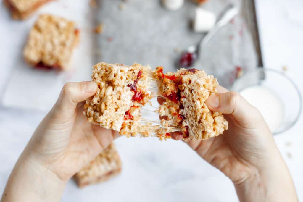 hands pulling apart two rice krispie treats with jelly in the middle