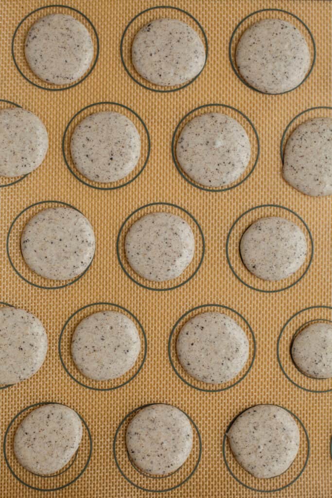 piped out macaron shells on a silicone mat