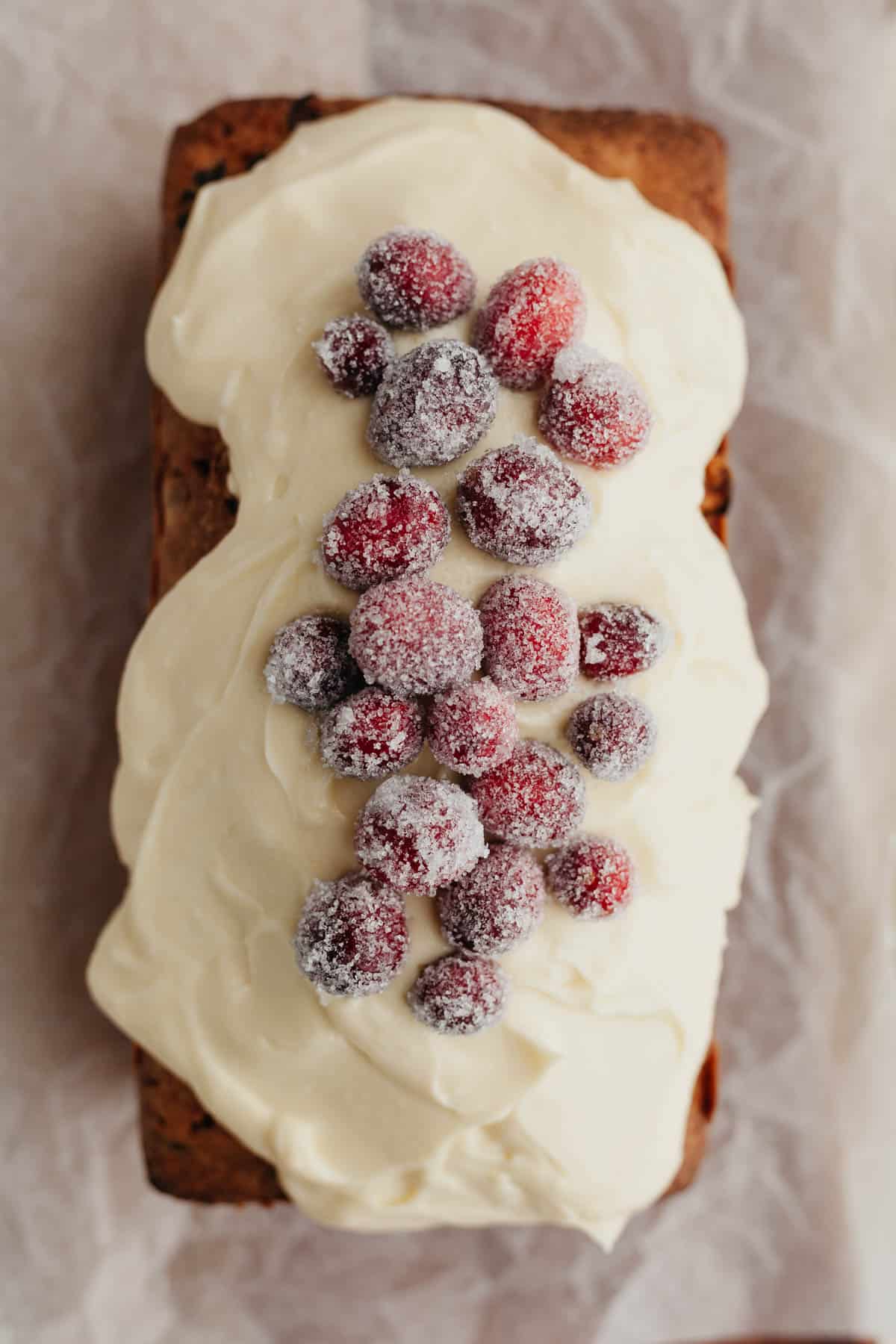 An overhead shot of a cranberry bread loaf, it is covered in white frosting and a row of sugared cranberries.
