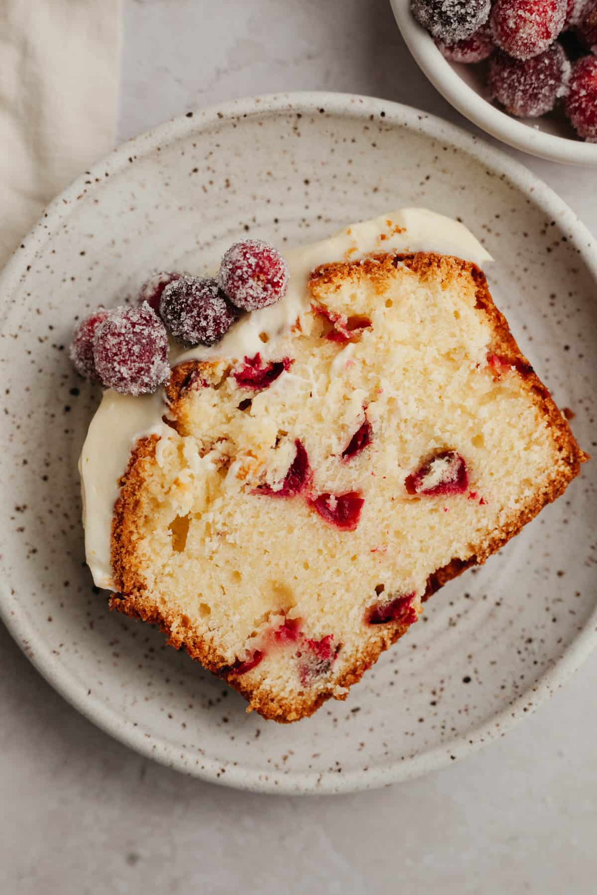A slice of cranberry lemon bread with white frosting on a small plate.
