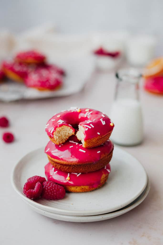 Three pink raspberry doughnuts on a small white plate