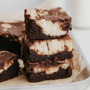 A stack of three cheesecake brownies on a silver baking tray.
