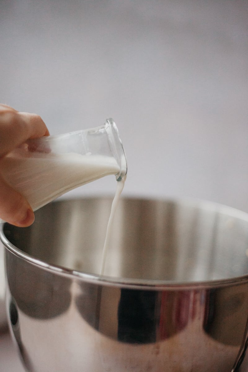 A small jug of milk being poured into a large metal bowl