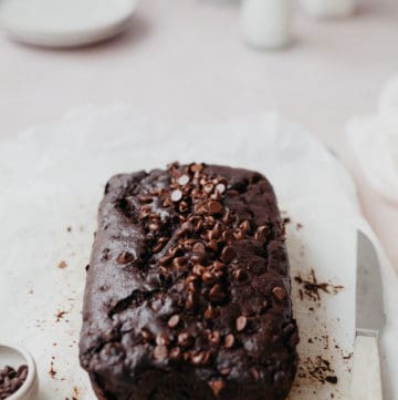 A baked chocolate sour cream pound cake on parchment paper with two jugs of milk behind