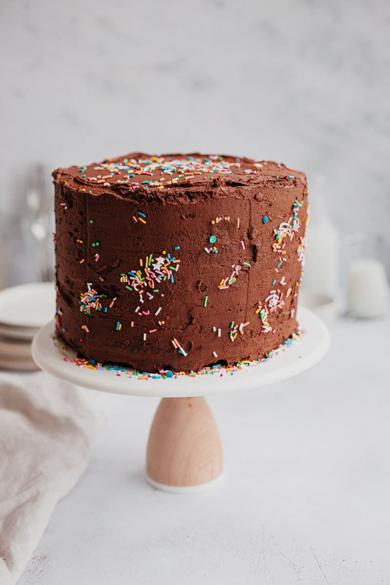 A chocolate frosted cake with sprinkles on a cake stand