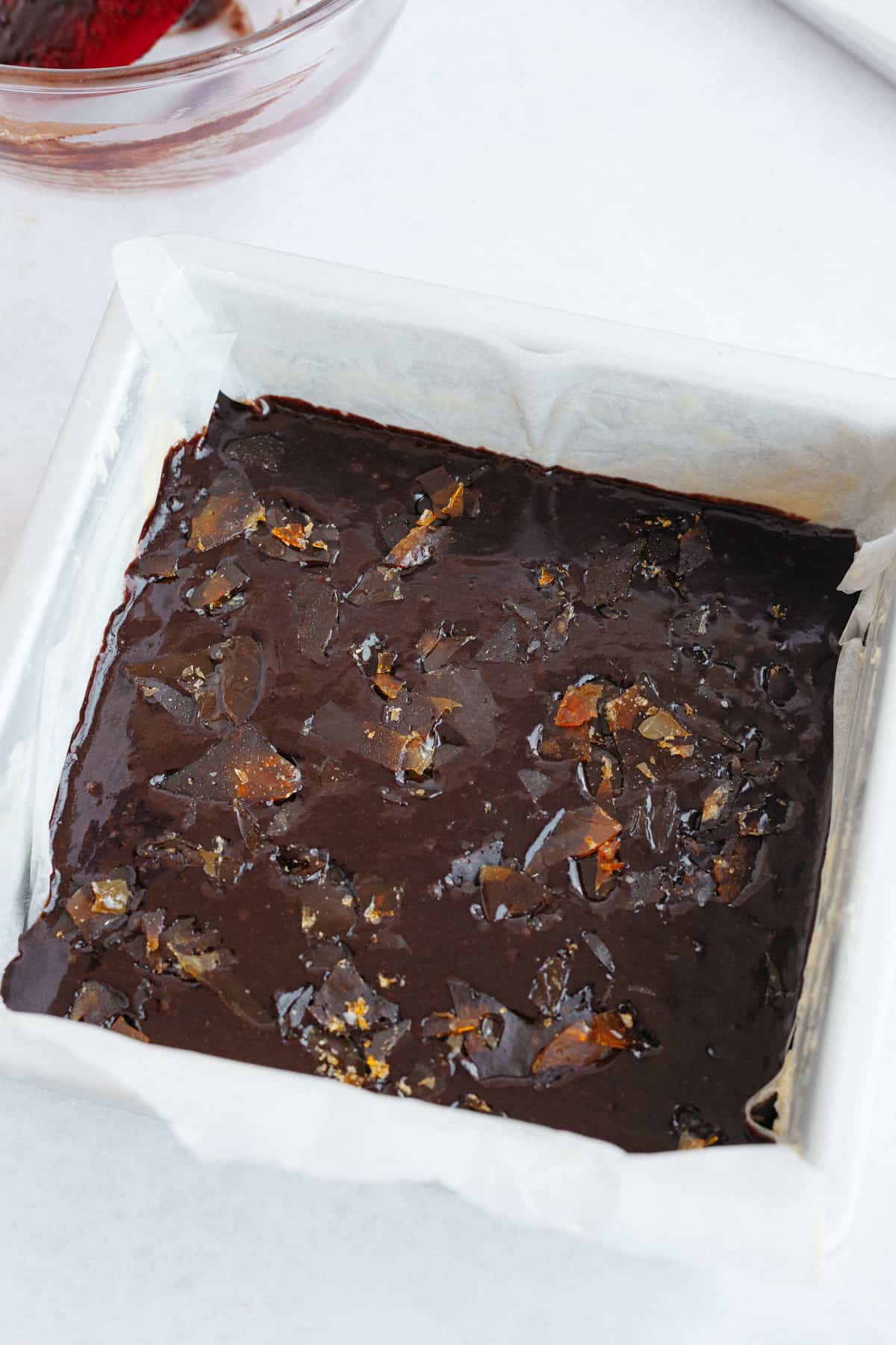 An 8x8 baking tin with unbaked brownie batter and caramel shards sprinkled on top