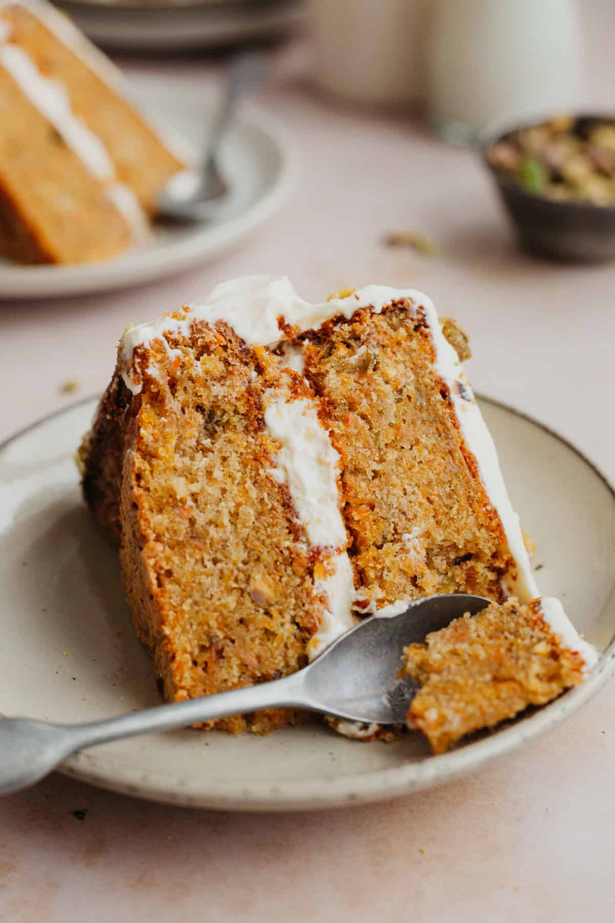 A slice of layered carrot cake with a small spoon scooping out a piece