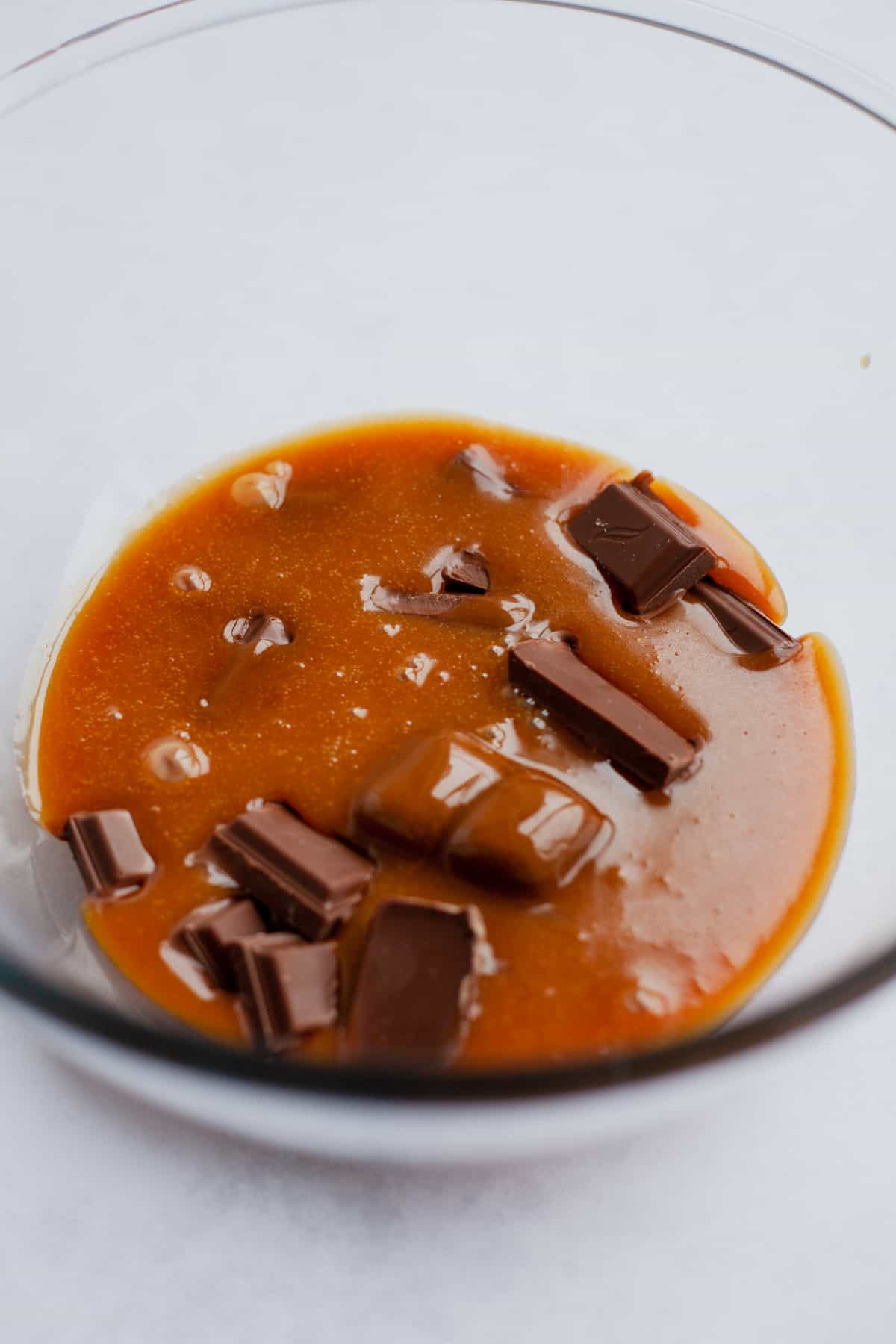 A clear pyrex bowl with chopped chocolate, covered in salted caramel.