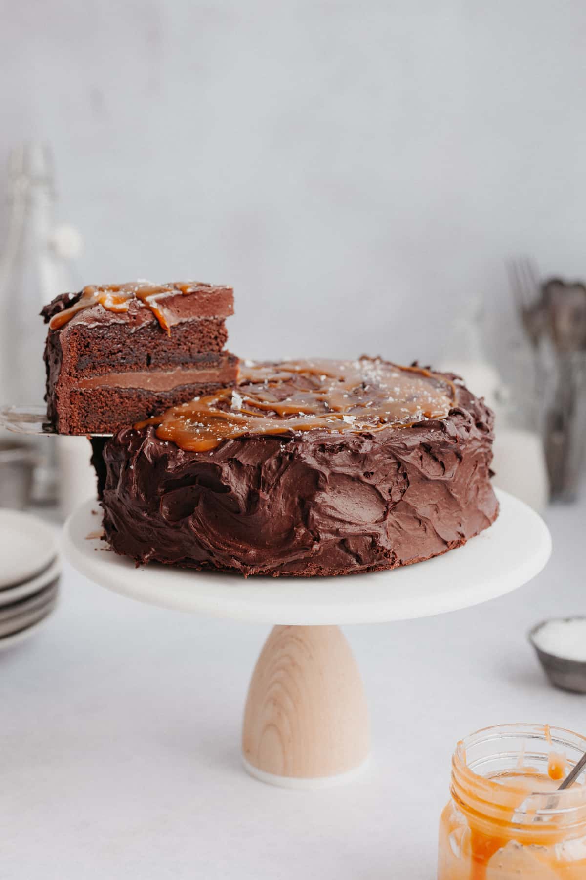 A chocolate cake with a caramel topping on a cake stand. One slice is being lifted out
