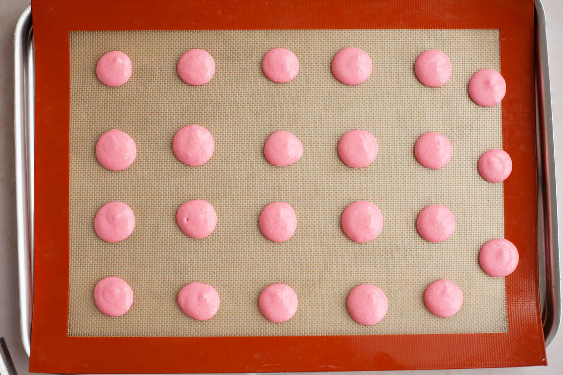 A baking tray with a silpat baking mat and piped out pink macaron shells, unbaked