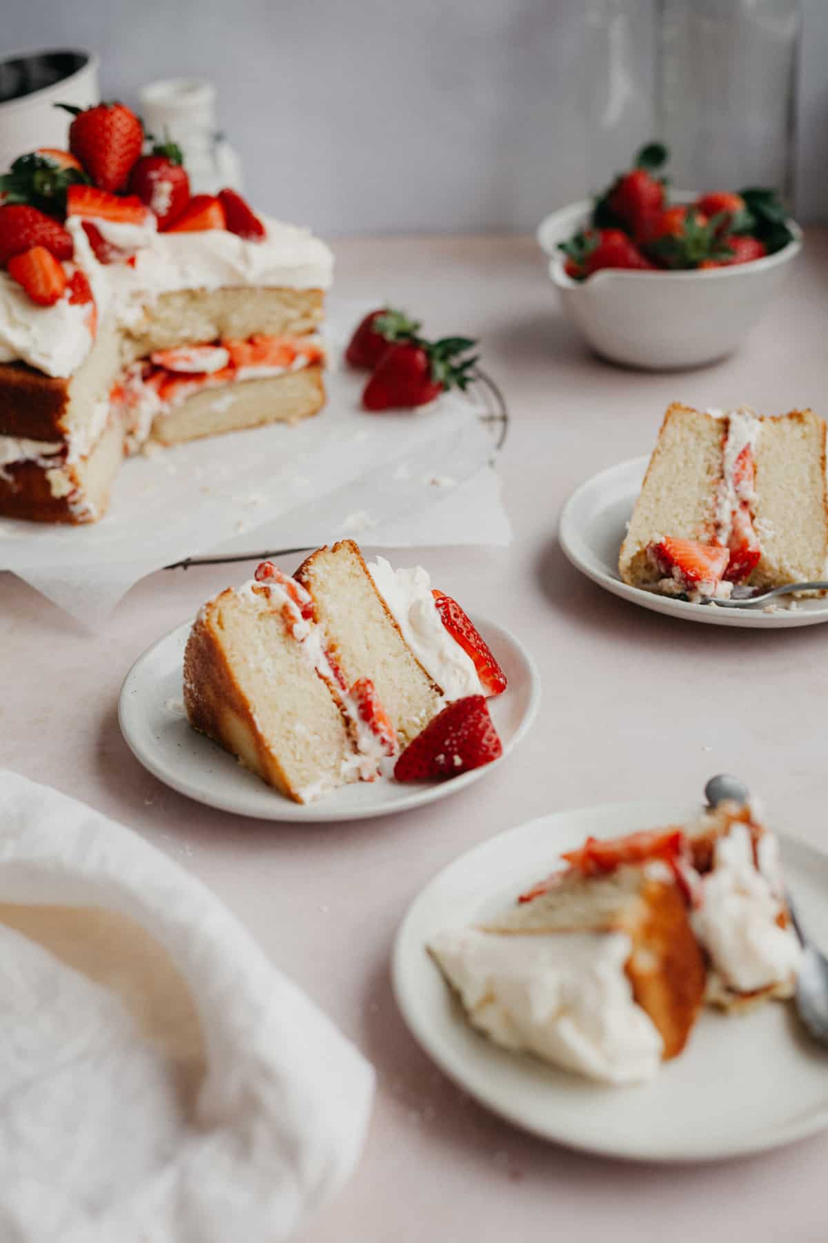 Three slices of white cake with strawberry filling on small beige plates.