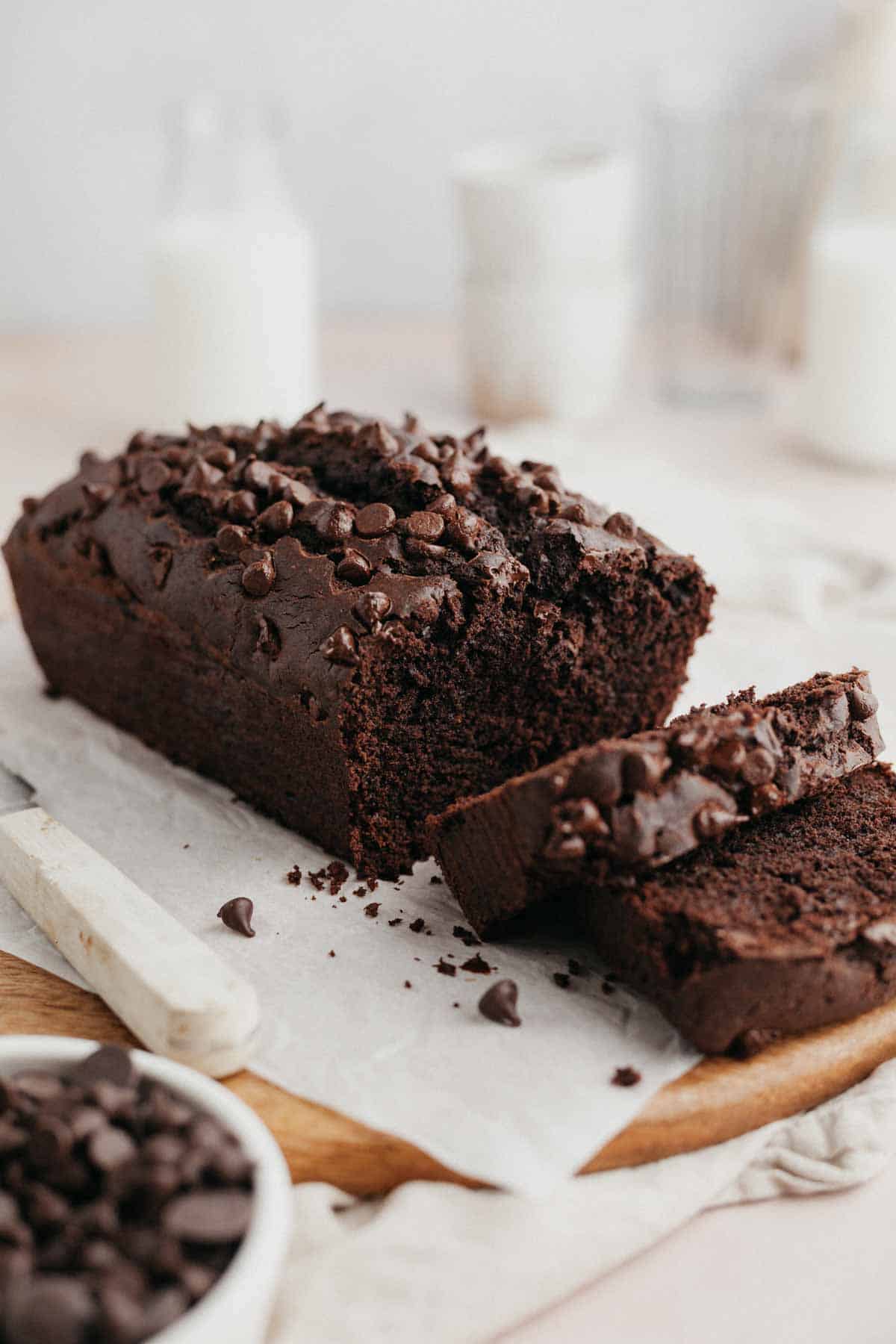 A chocolate pound cake covered with chocolate chips on parchment paper, 2 slices have been cut.