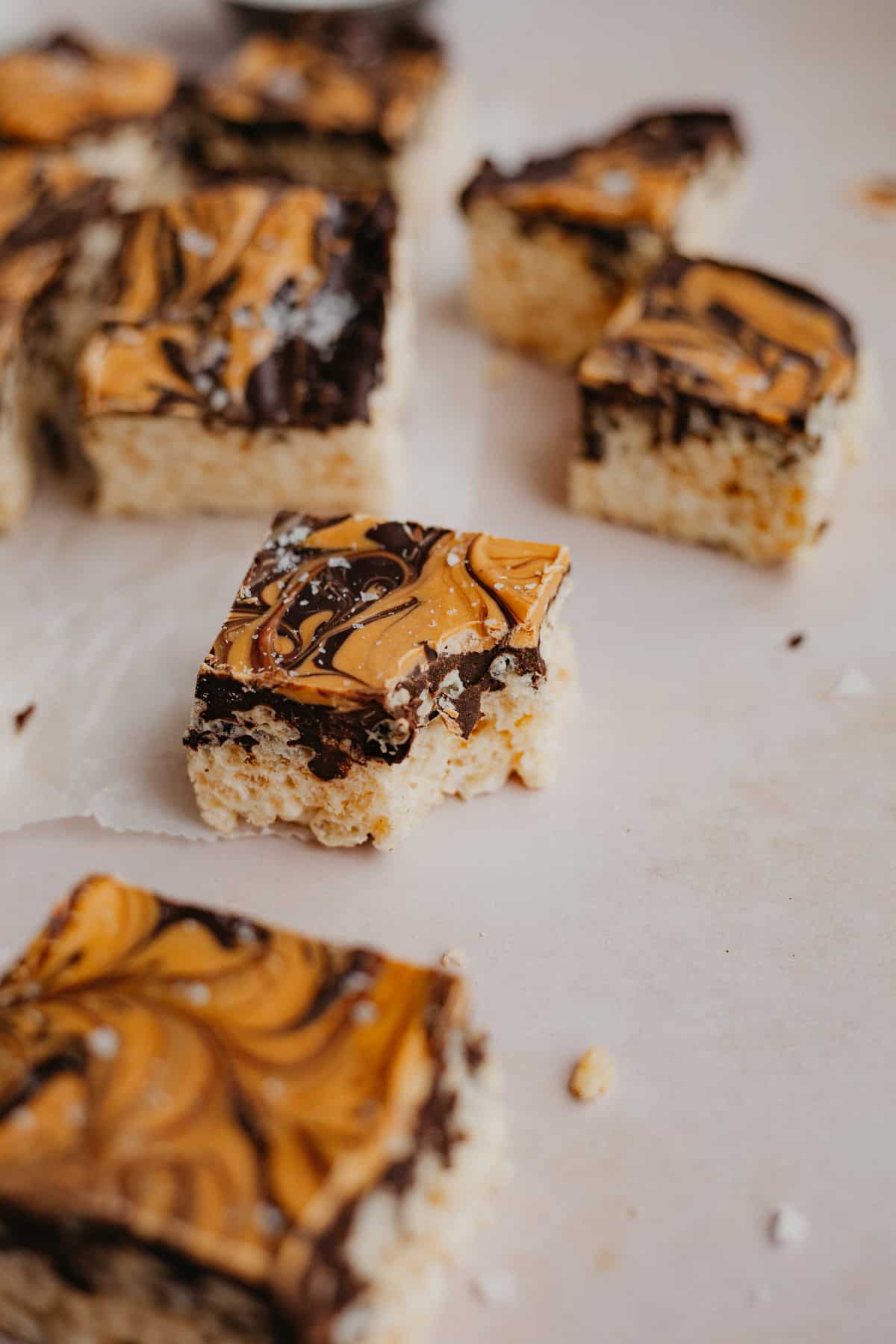 Several chocolate covered rice krispie treats cut into squares on parchment paper. One square has a bite taken out of it.