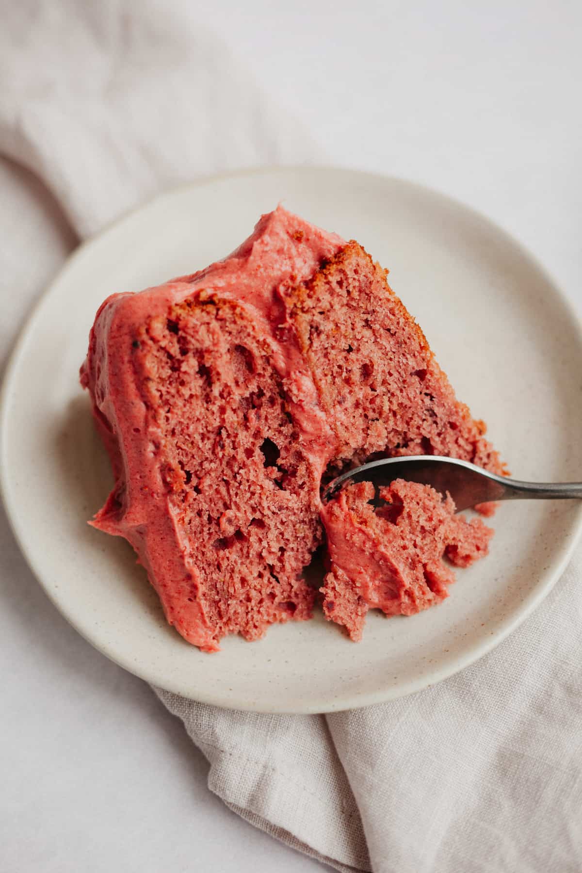 A slice of strawberry pink cake on a small beige plate