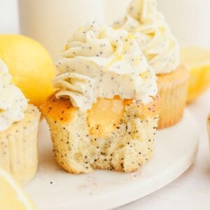 A close up of a lemon poppy seed cupcake with a bite taken out of it, showing there is lemon curd in the middle of the cupcake.