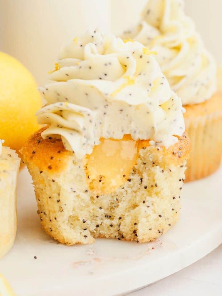 A close up of a lemon poppy seed cupcake with a bite taken out of it, showing there is lemon curd in the middle of the cupcake.