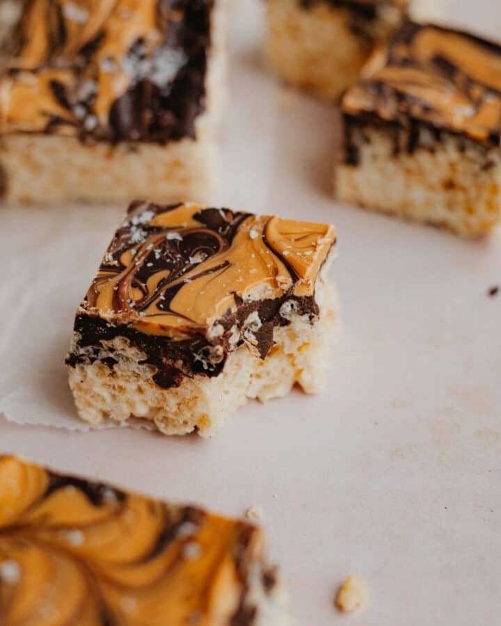 Several chocolate covered rice krispie treats cut into squares on parchment paper. One square has a bite taken out of it.