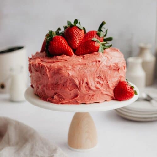 A pink strawberry cake frosted with strawberry frosting on a white cake stand