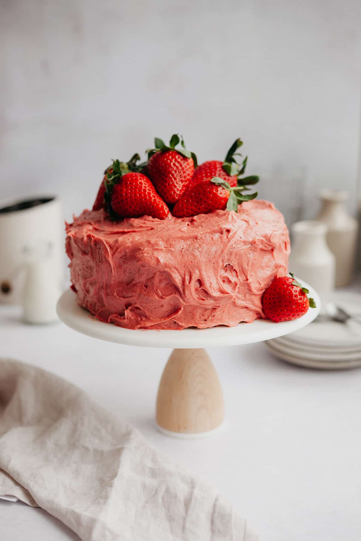 A pink strawberry cake frosted with strawberry frosting on a white cake stand