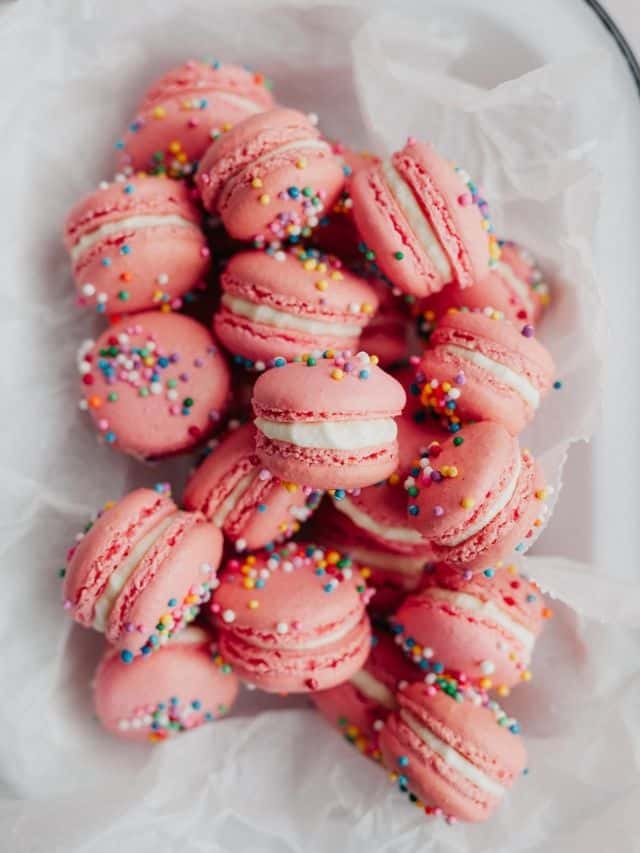 pink macarons covered in rainbow nonpareil sprinkles in parchment paper