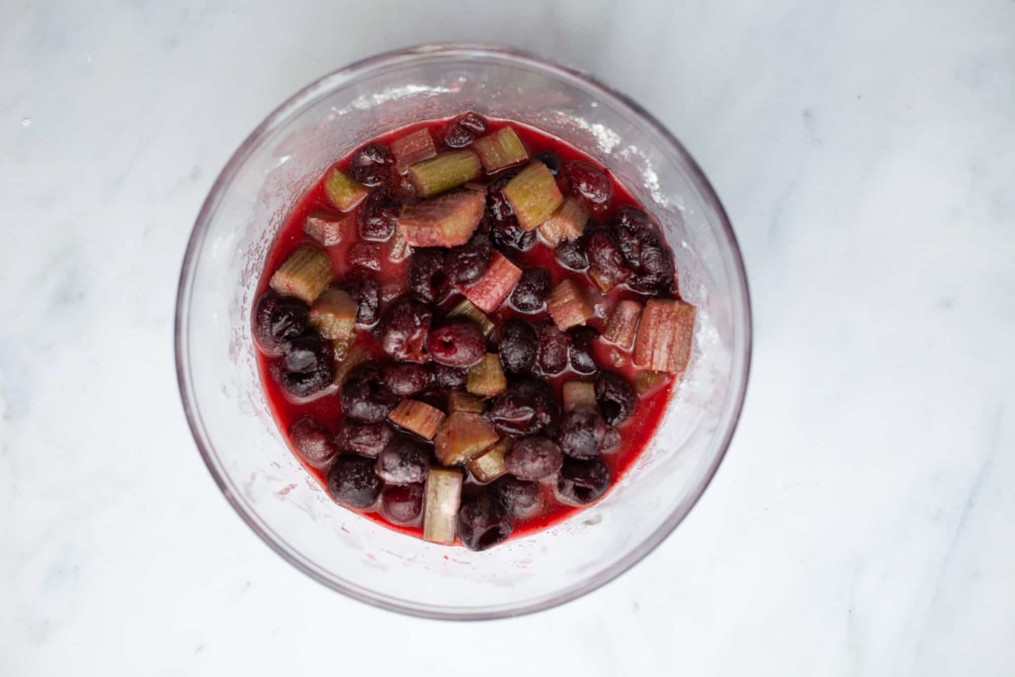 A pyrex mixing bowl with cherries, cut rhubarb and their juice