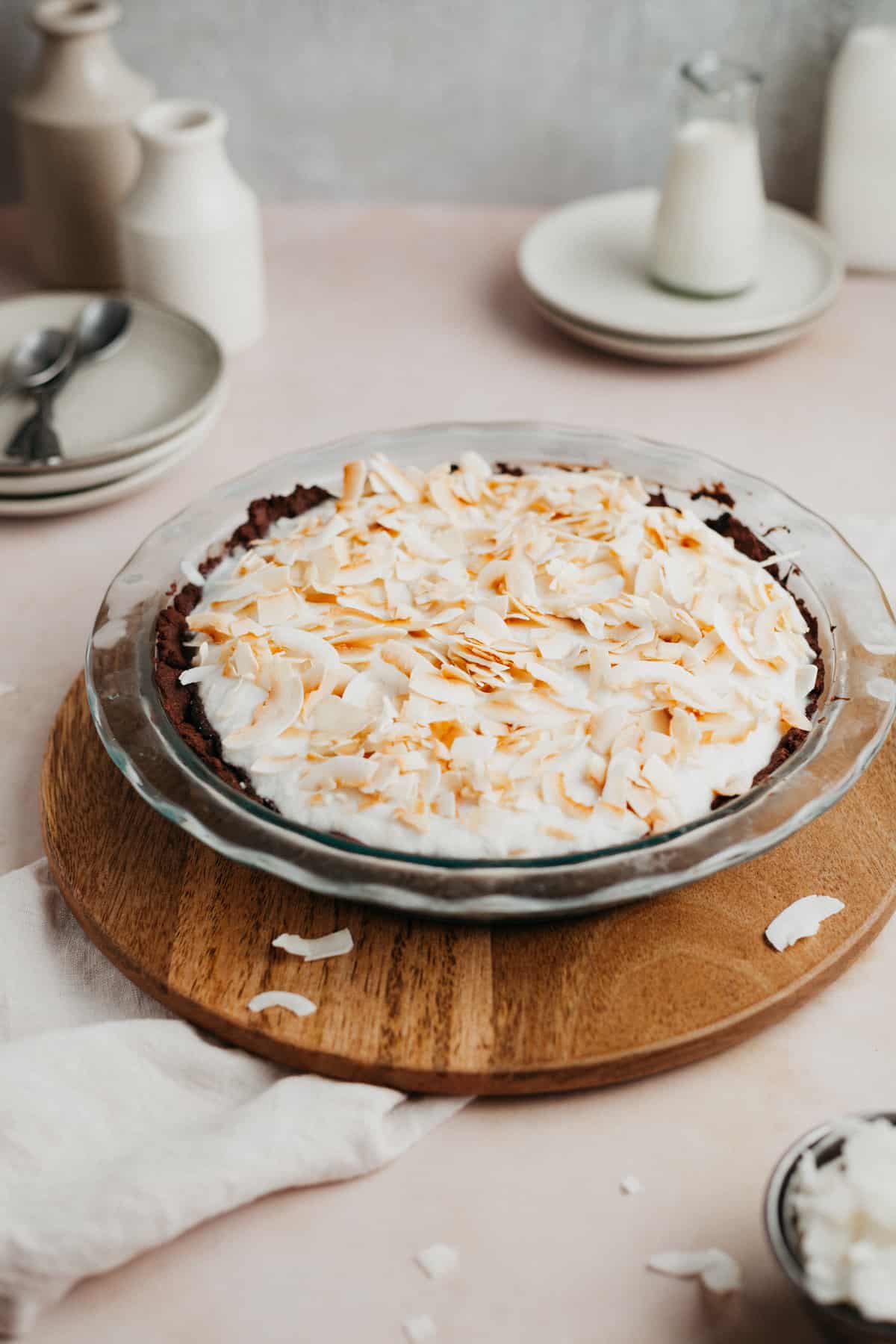 A chocolate pie topped with whipped cream and toasted coconut in a pyrex pie plate.