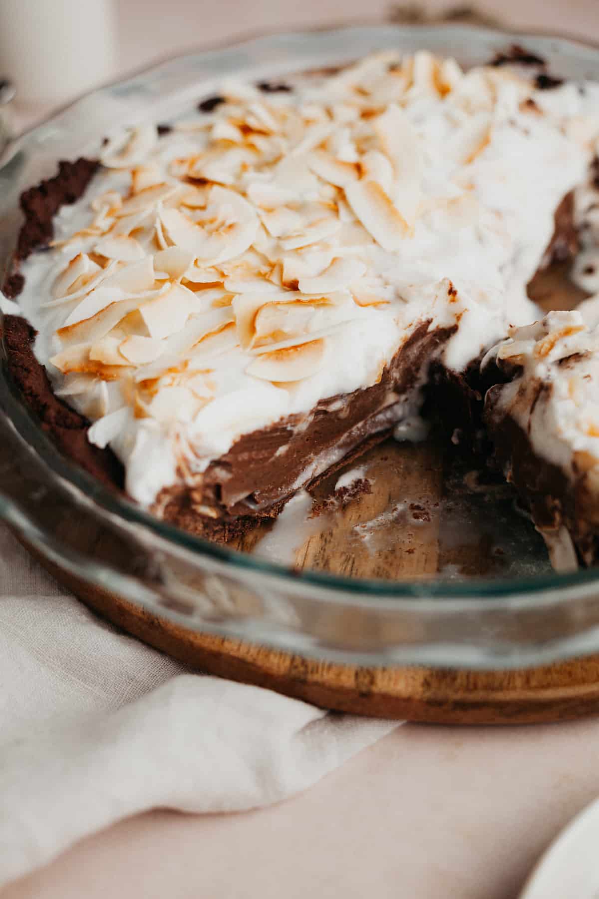 A chocolate pie topped with whipped cream and toasted coconut in a pyrex pie plate. A few slices have been taken out