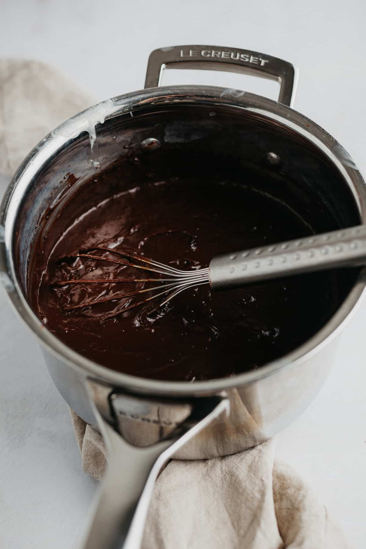 Chocolate custard in a silver saucepan with a small silver whisk
