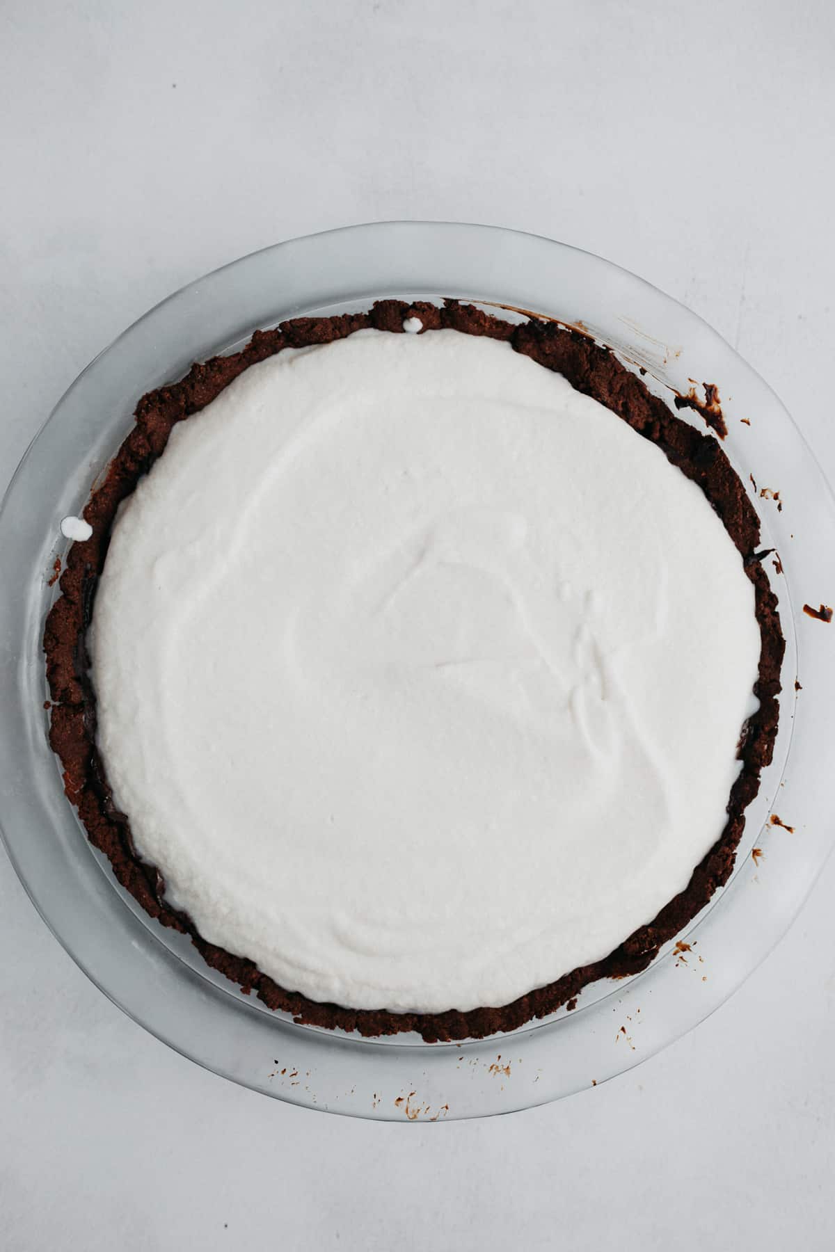 A pyrex pie plate with a chocolate cookie crust. It is covered in white coconut whipped cream