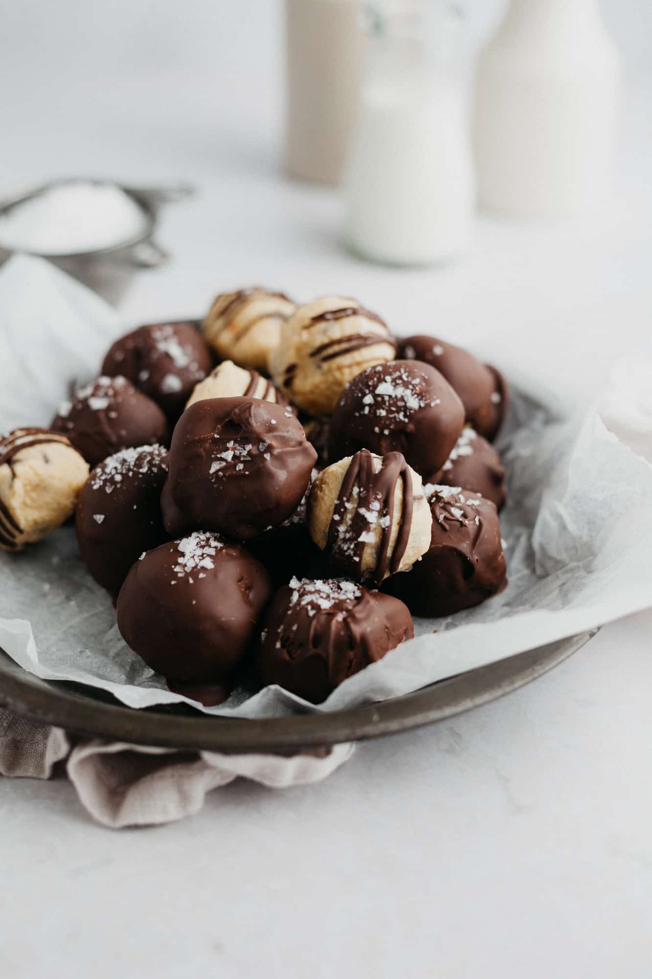 Cookie dough bites dipped in chocolate and sprinkled with sea salt on parchment paper. One has a taken out of it