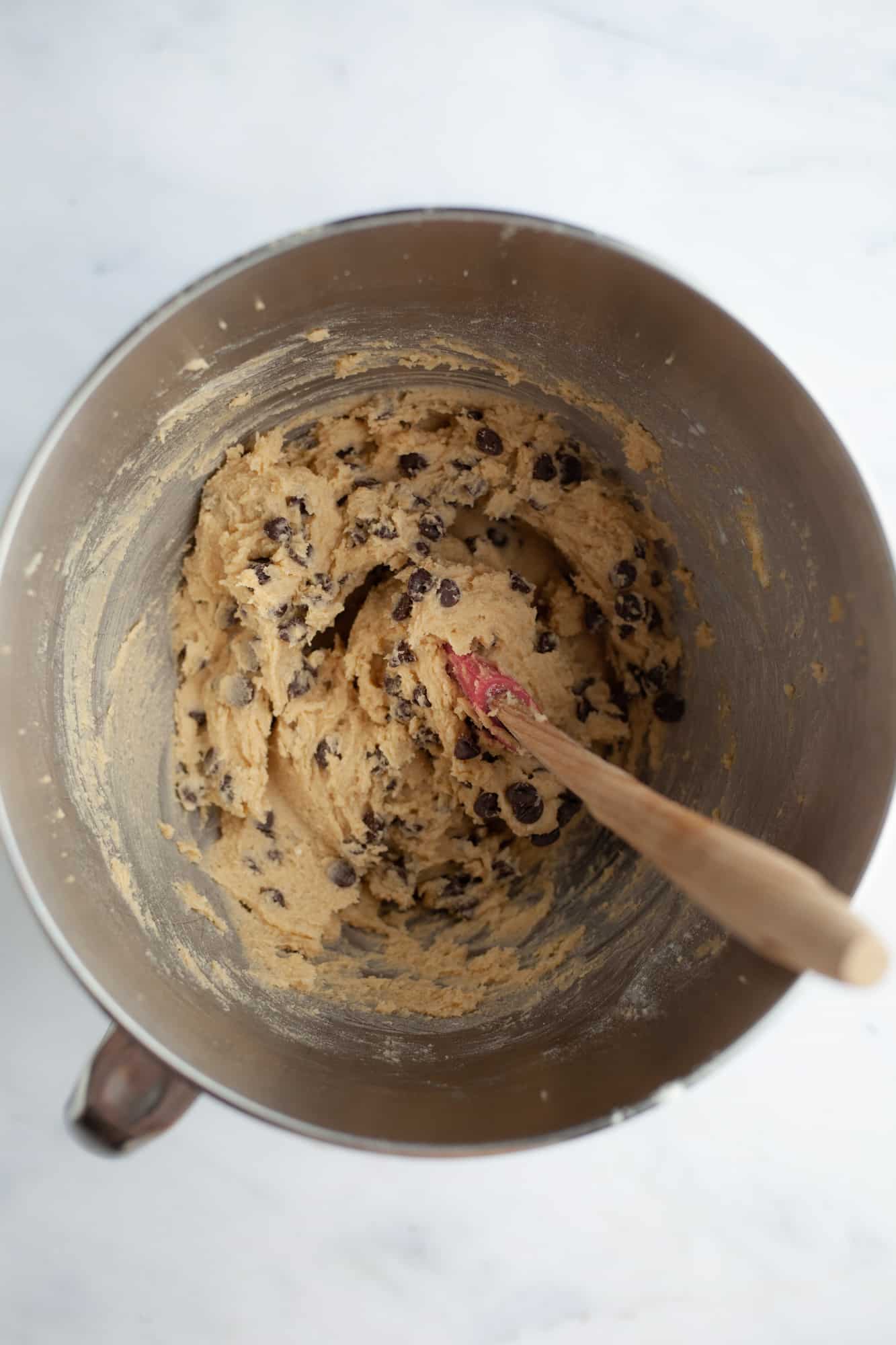 An overhead shot of a silver mixing bowl with cookie dough batter and chocolate chips