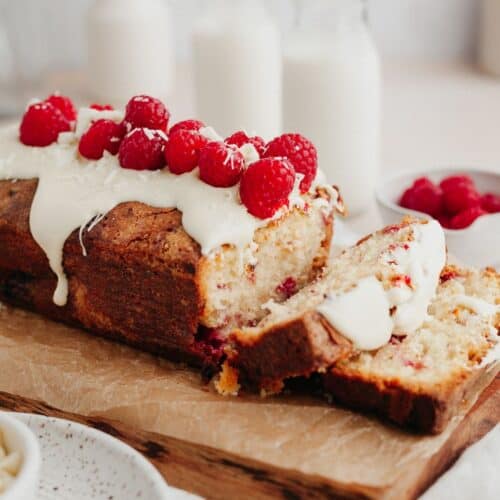 A raspberry white chocolate loaf cake covered in melted white chocolate and fresh raspberries, two slices have been cut.
