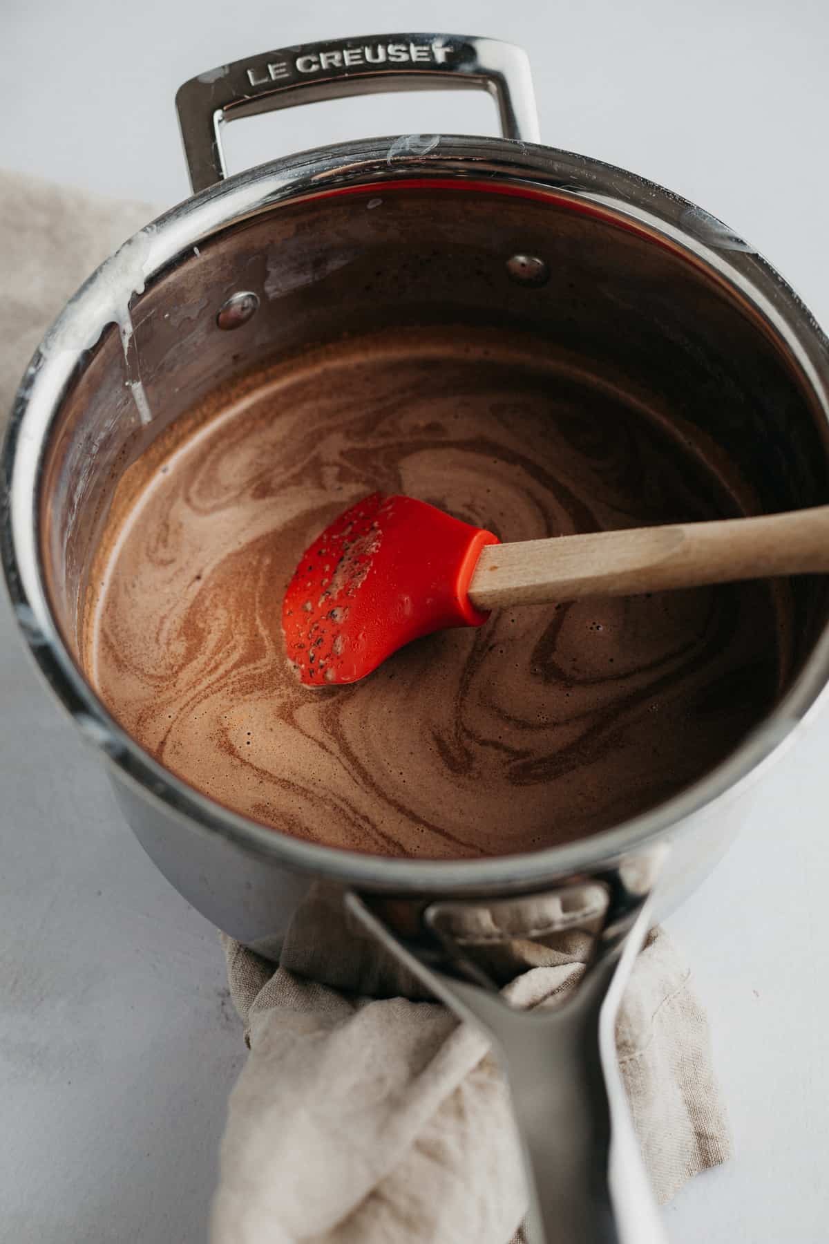 Chocolate custard in a silver saucepan with a small silver whisk