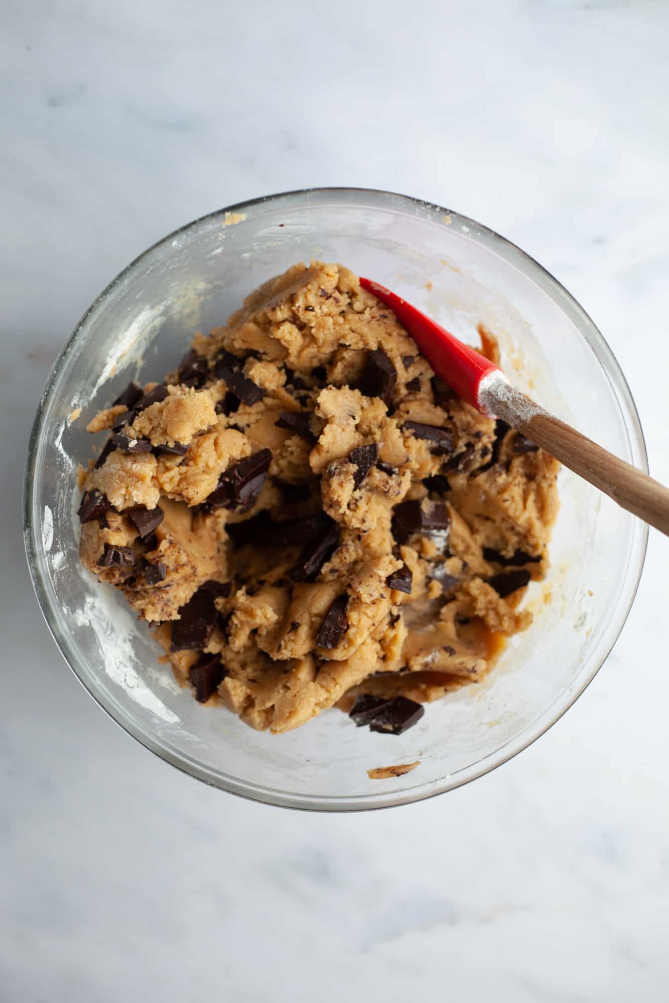 Chocolate chip cookie dough in a pyrex bowl with a wooden spatula