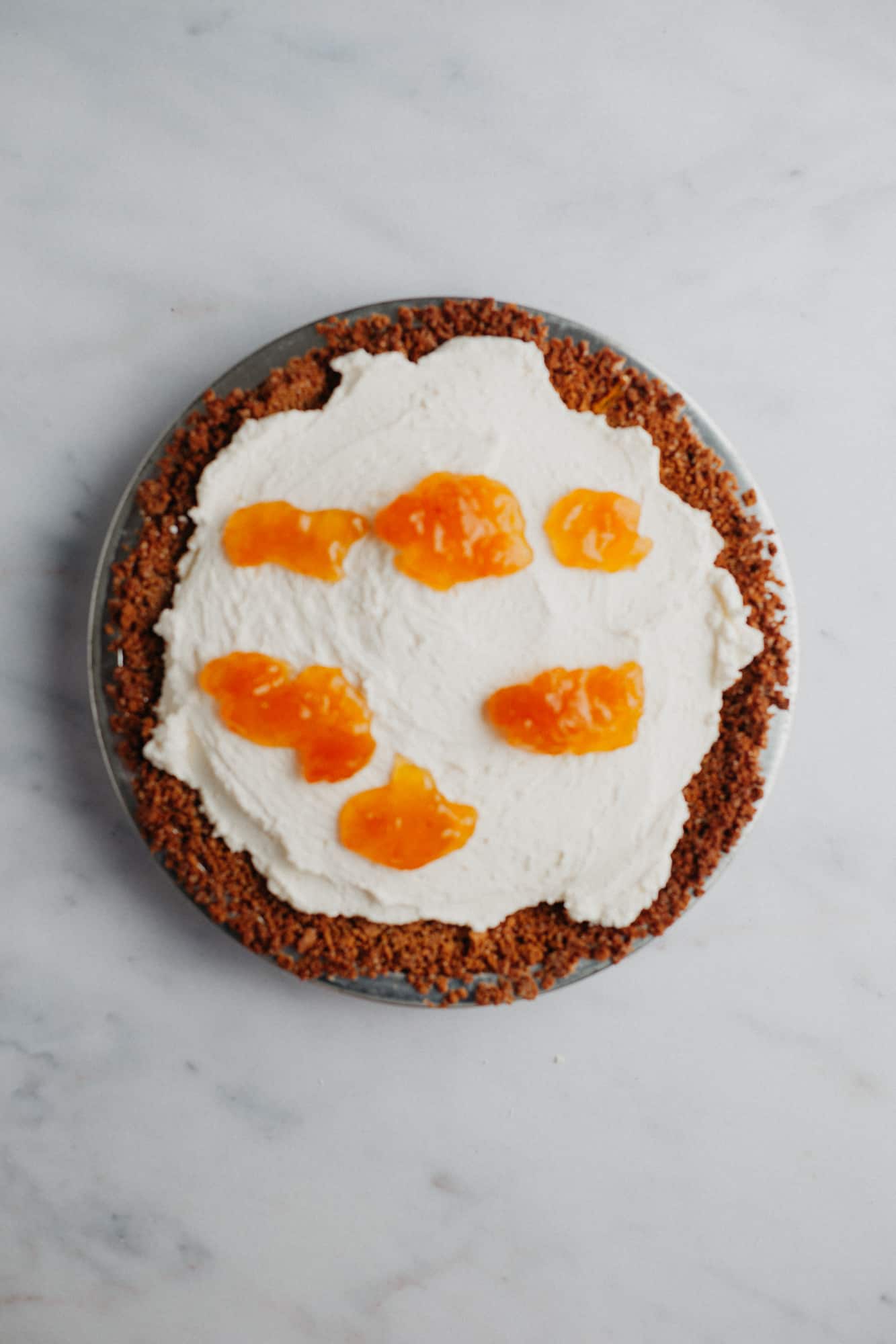A graham cracker crust with a mascarpone cream filling. There are six dollops of peach jam on top