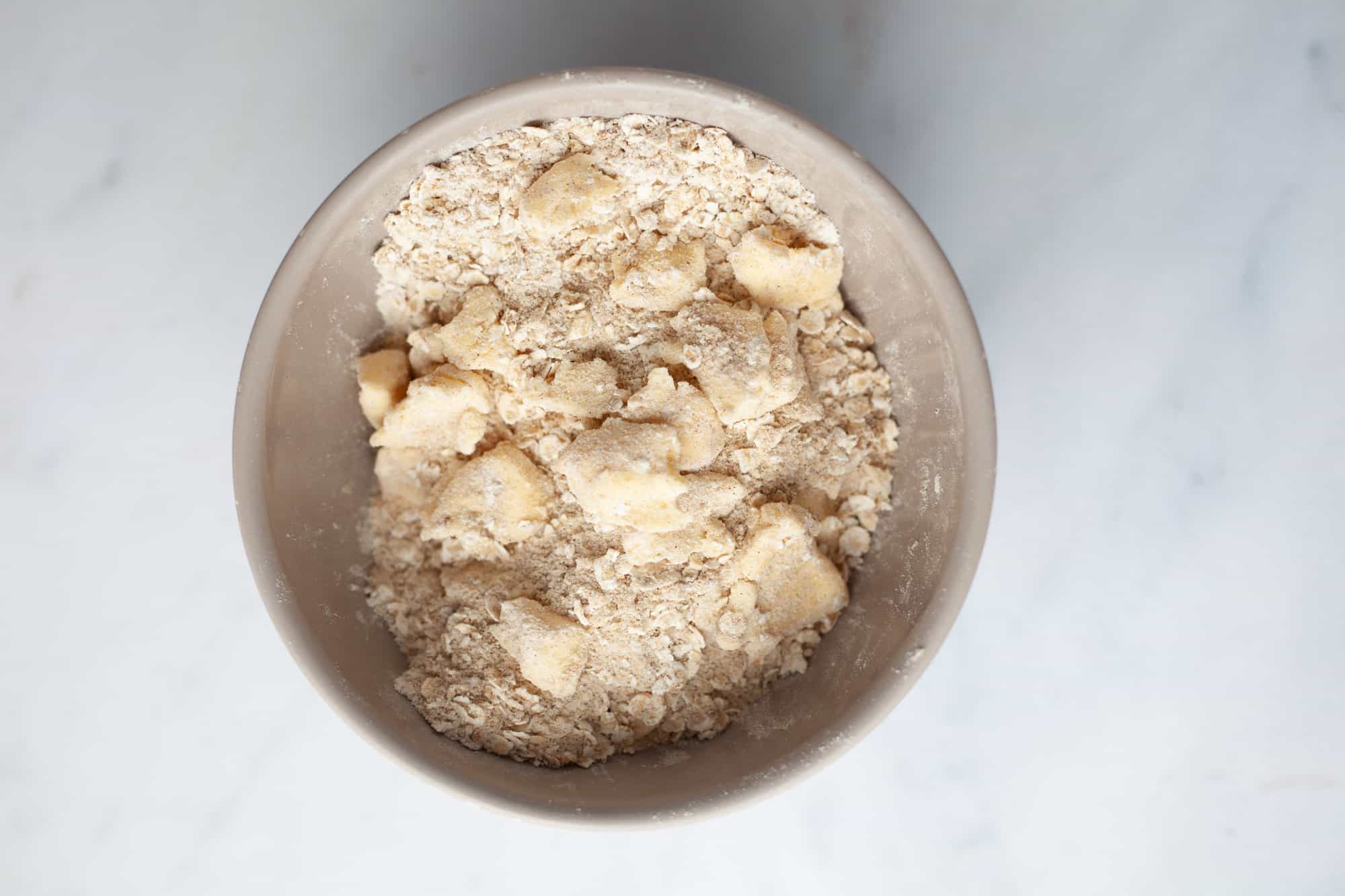 A small beige bowl with what looks like flour, oats, and small bits of butter