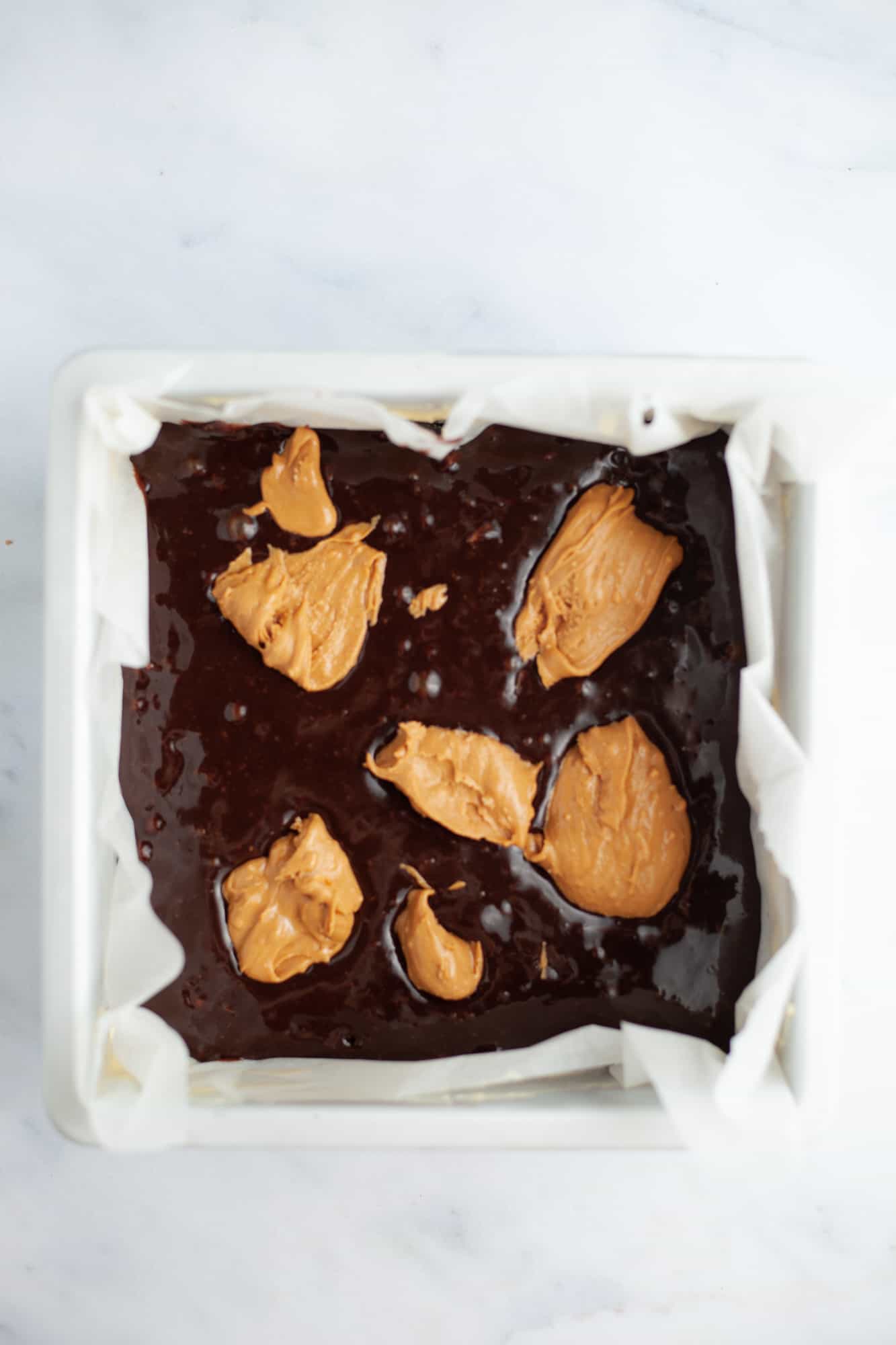Brownie batter in a square pan with dollops of peanut butter