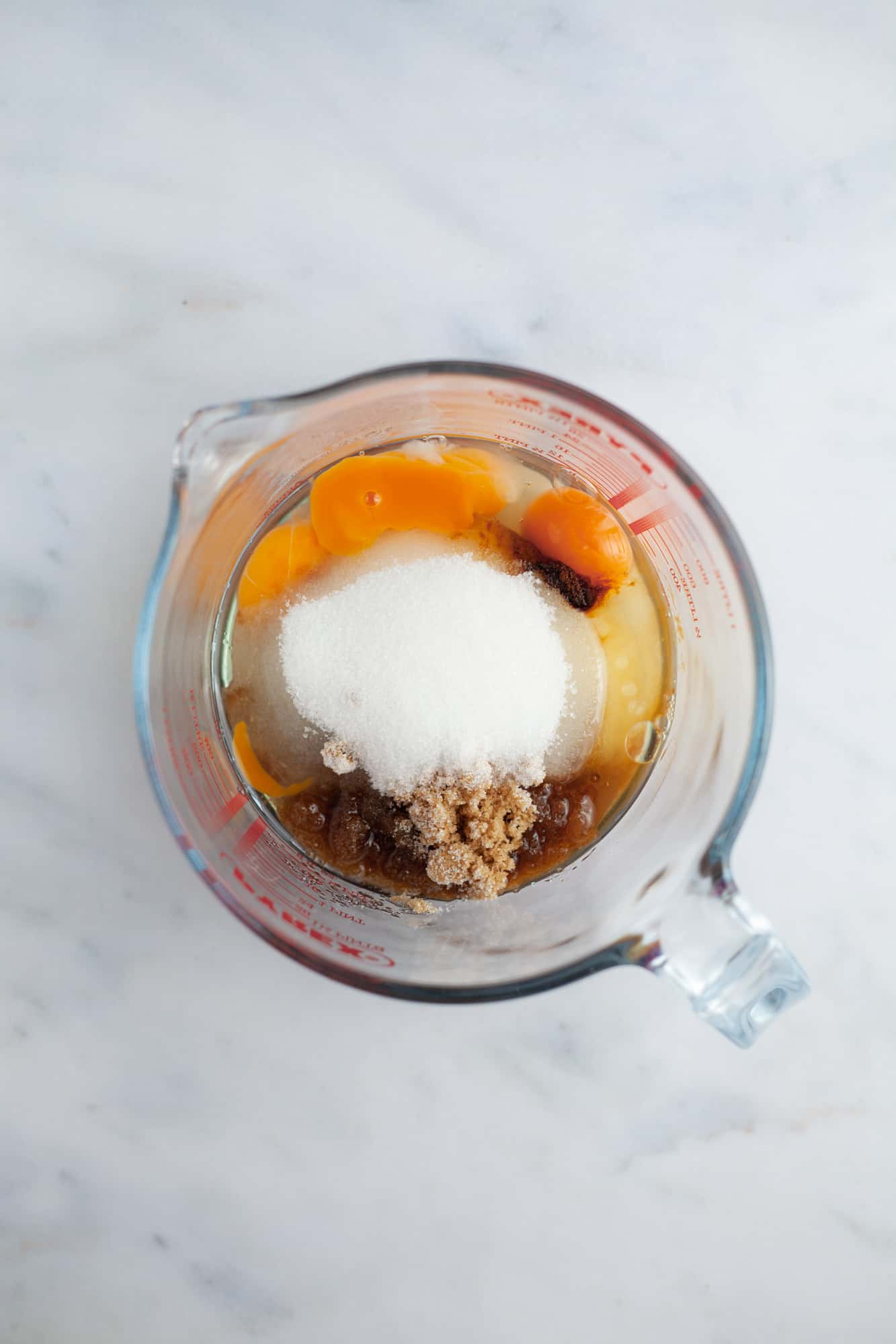 A glass pyrex jug with light brown sugar, sugar, three eggs and vanilla