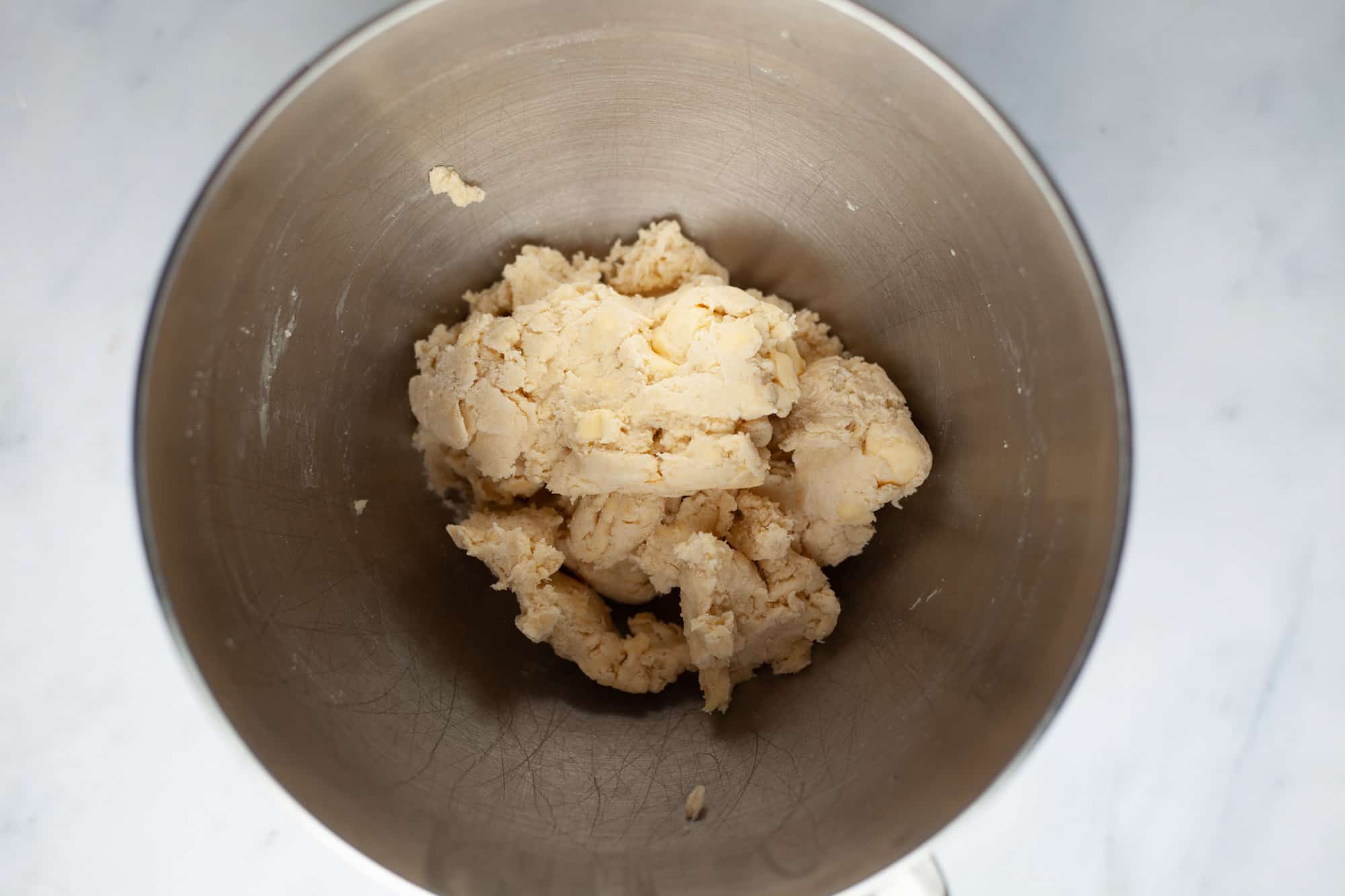 An overhead shot of pie dough in a silver mixing bowl