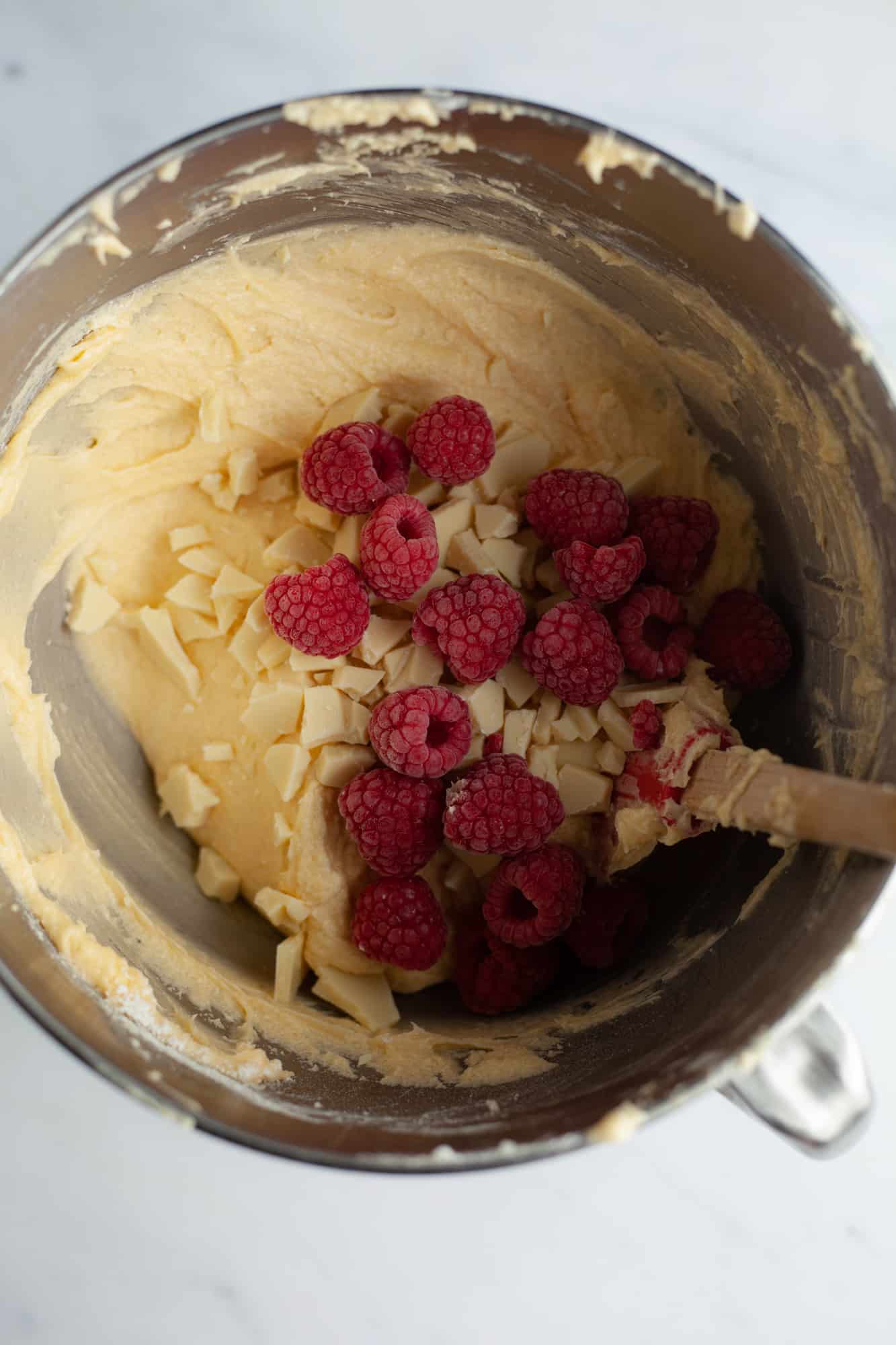 Cake batter, raspberries and white chocolate chunks in a large silver bowl