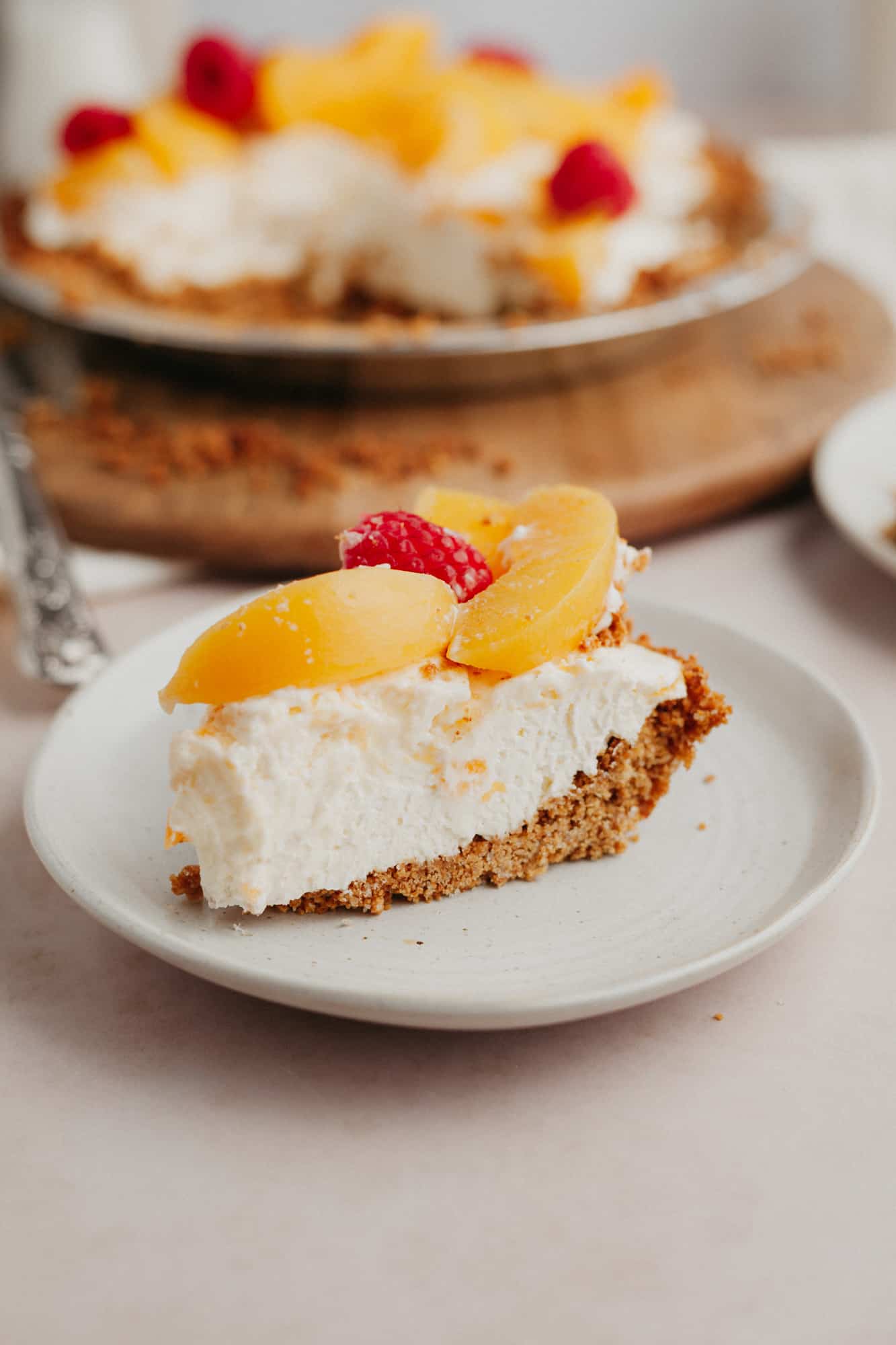 A slice of no bake peach pie on a small beige plate, topped with sliced peaches.