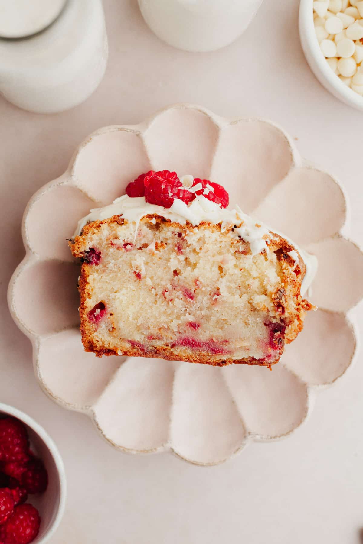 A slice of white chocolate raspberry cake on a scalloped pink plate.