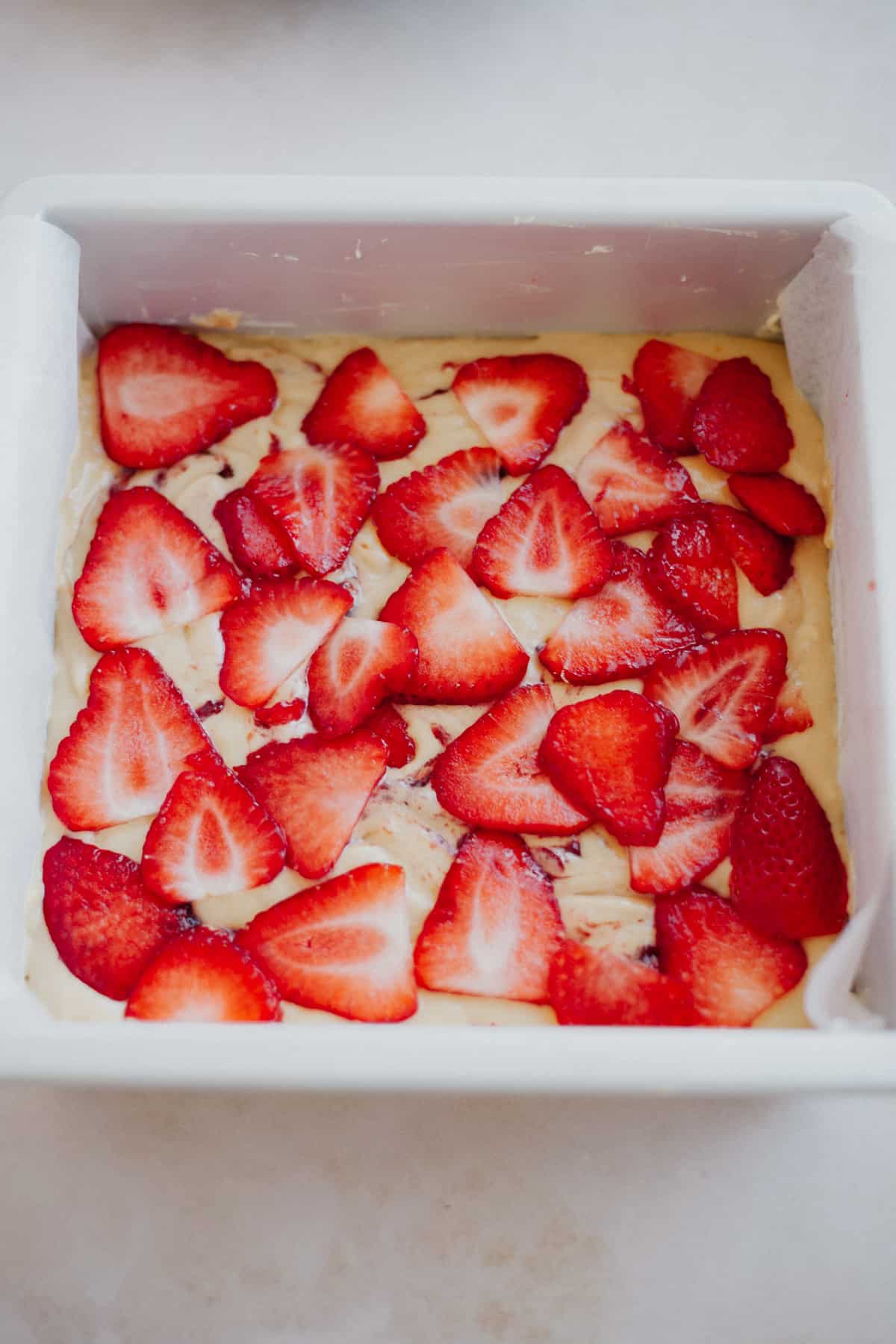 A cake pan with cake batter, the batter is topped with very thinly sliced strawberries.