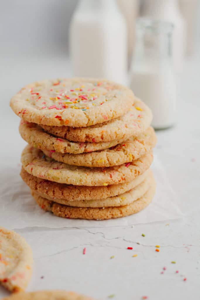 A stack of sprinkle sugar cookies, with two small bottles of milk behind them