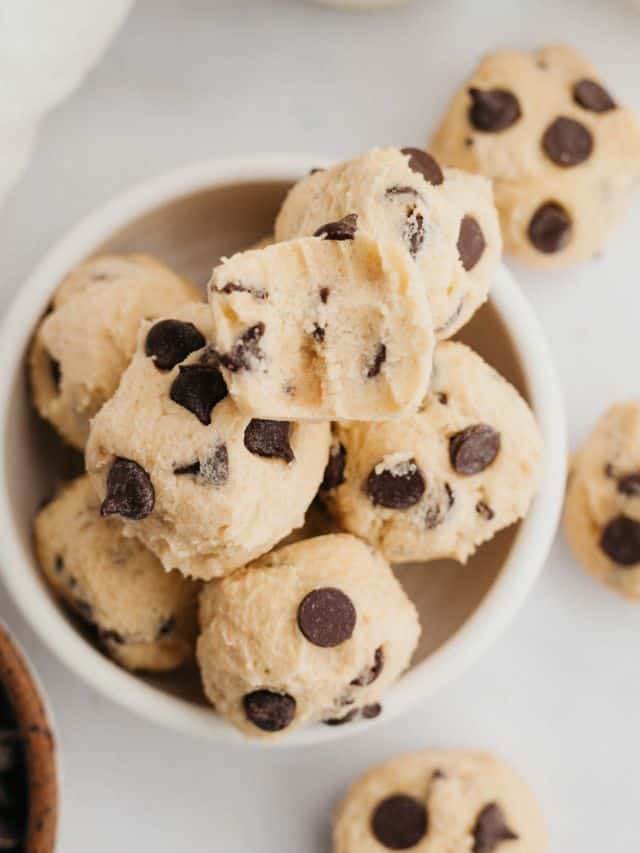 edible cookie dough bites in a small white bowl, one has a bite taken out of it.