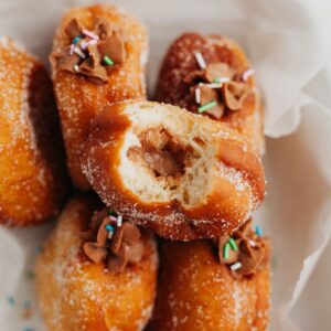 Five brioche doughnuts on top of parchment paper. One doughnut is on top, a bite taken out of it showing a chocolate filling